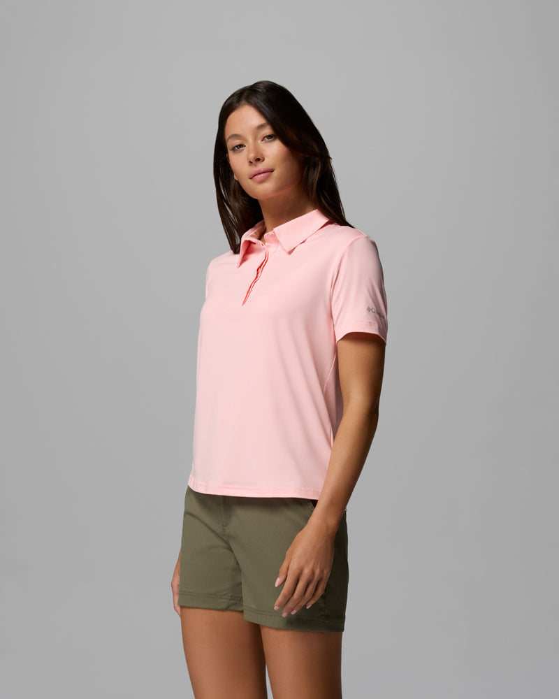 A woman models the Parsons Point Polo W, a light pink women's polo shirt, with olive green shorts against a gray background.