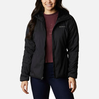 אישה לבושה במעיל Softshell שחור מדגם Kruser Ridge II של ColumbiaIL, מעל חולצה בצבע בורדו וג'ינס כהה, מחייכת בעודה עומדת על רקע לבן חלק.